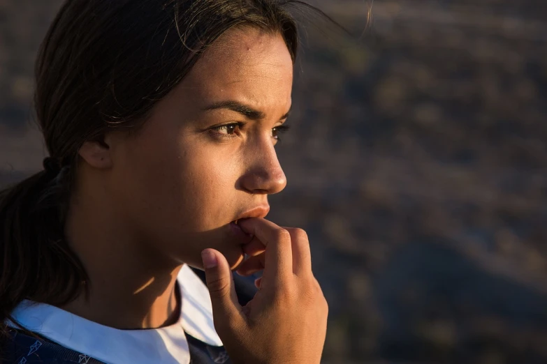 a close up of a person eating a banana, by Christen Dalsgaard, antipodeans, girl watching sunset, mixed race woman, prominent jawline, eerie moorlands behind her