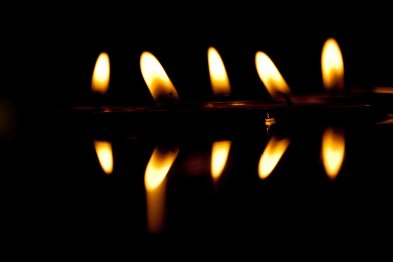 a group of lit candles sitting on top of a table, a picture, by Jan Rustem, minimalism, fire reflection, abstract photography, in a row, flash photo
