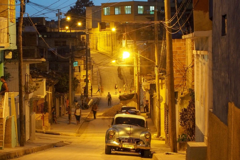 a car driving down a street at night, a photo, flickr, colombian, movie set”, hill, golden hour”