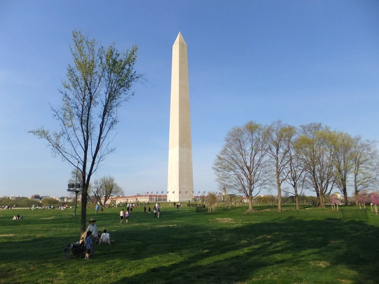 a group of people sitting on top of a lush green field, a picture, by Samuel Washington Weis, flickr, obelisk, park on a bright sunny day, trump, seen from the side