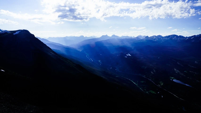 a group of people standing on top of a mountain, a picture, by Andrew Domachowski, minimalism, light rays and shadows, banff national park, distant valley, blue river in the middle