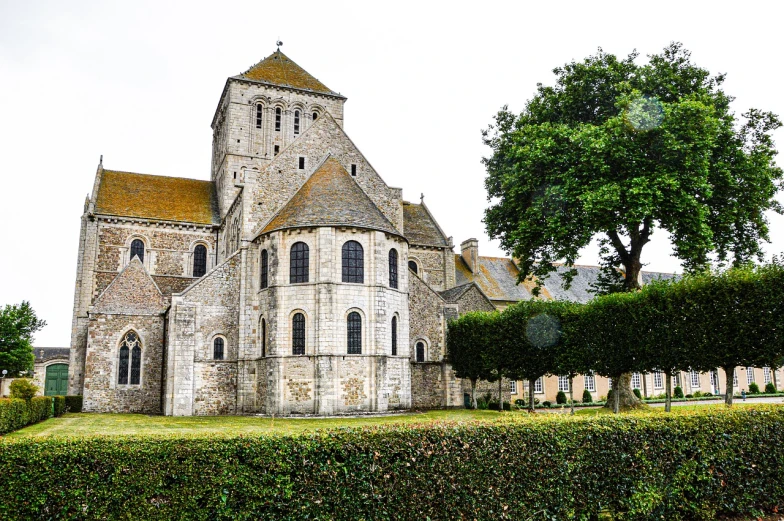 a large stone building sitting next to a lush green hedge, a photo, by Etienne Delessert, romanesque, normandy, church cathedral, on a cloudy day, marine