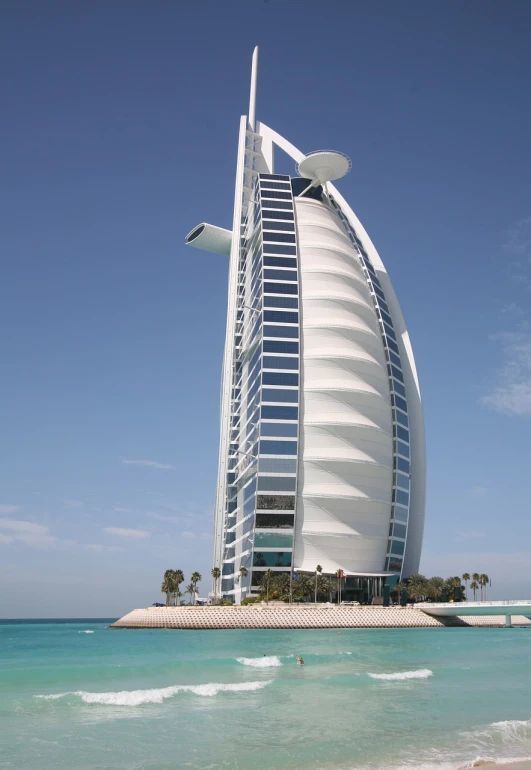 a tall building sitting on top of a beach next to the ocean, by Sheikh Hamdullah, shutterstock, hurufiyya, sails, vertical architecture, nautilus, taken with a pentax k1000