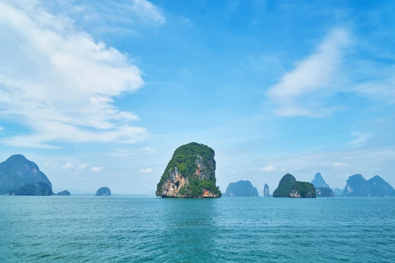 a large rock formation in the middle of a body of water, a tilt shift photo, thailand, very beautiful photo, distant photo, clear summer sky background