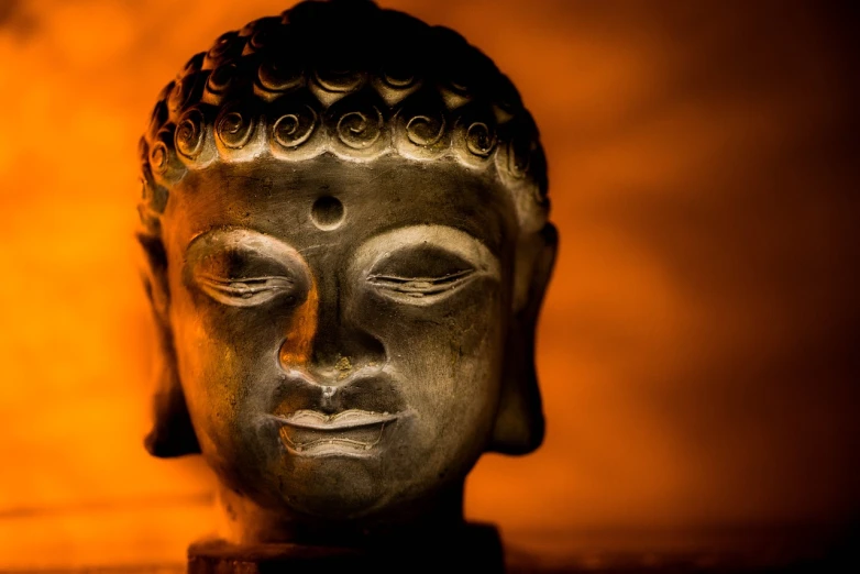 a close up of a statue of a person's face, pexels, hindu stages of meditation, in front of an orange background, sacred perfect lighting, the buddha