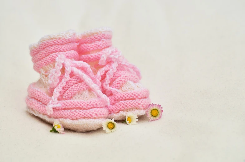 a pair of pink baby shoes on a white surface, realism, made of wool, spring theme, close up portrait photo, summer setting