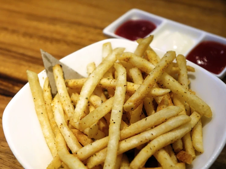 a white plate topped with french fries next to ketchup, inspired by Pia Fries, closeup - view, pepper, trio, a wooden