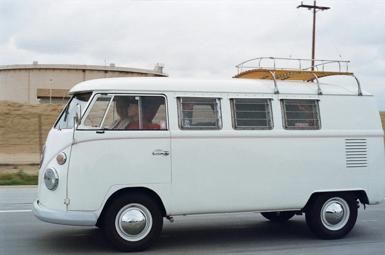 a white van driving down a street next to a building, by Dennis Ashbaugh, unsplash, modernism, vw microbus driving, wikimedia commons, large open windows, hooded