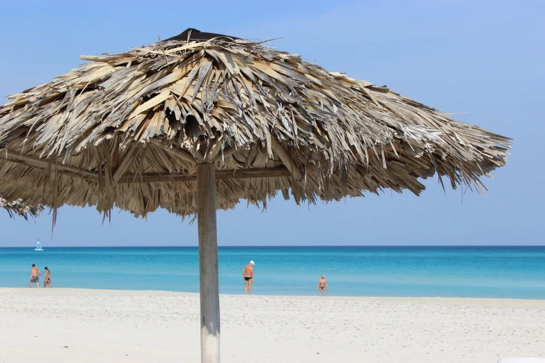 a thatched umbrella sitting on top of a sandy beach, a picture, pixabay, minimalism, varadero beach, 30-year-old woman from cuba, beach in the foreground, older male