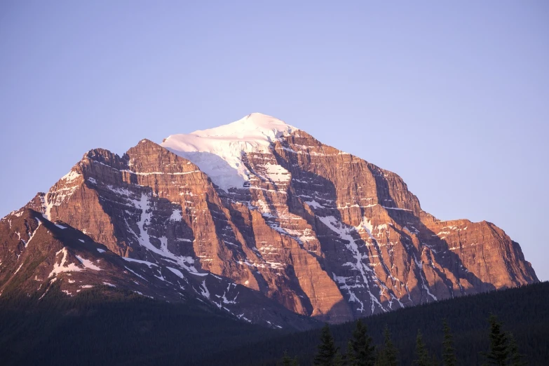 a snow covered mountain with pine trees in the foreground, a picture, by George Claessen, shutterstock, minimalism, late afternoon sun, banff national park, shiny layered geological strata, stock photo