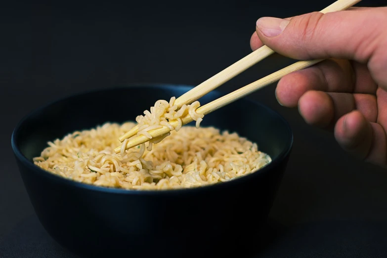 a person holding chopsticks over a bowl of noodles, a stock photo, by Matthias Stom, with a black background, closeup photo, miniature product photo, eating ramen