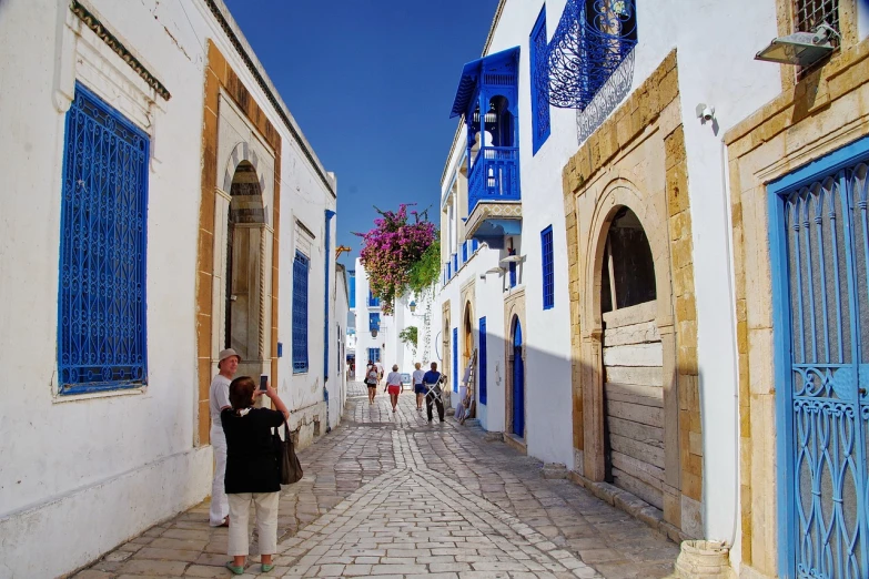 a woman taking a picture of a narrow street, a photo, flickr, blue white colors, cyprus, moroccan mosque, travelers walking the streets