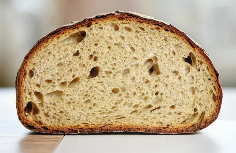 a piece of bread sitting on top of a table, by David Simpson, reddit, mingei, side view close up of a gaunt, soft internal light, malt, gold speckles
