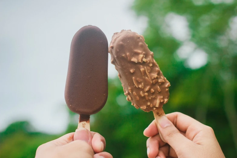 a person holding a chocolate covered ice cream on a stick, unsplash, istockphoto, male and female, brown resin, 🐿🍸🍋