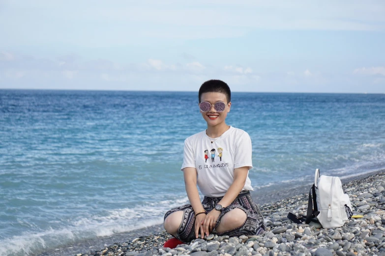 a boy sitting on a rocky beach next to the ocean, a picture, inspired by Pan Tianshou, wearing a t-shirt, with sunglass, queen of the sea mu yanling, high-resolution photo