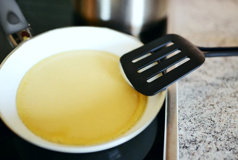 a close up of a pan on a stove with a spatula, a pastel, by Dietmar Damerau, shutterstock, bauhaus, living food adorable pancake, melted cheddar, smooth surface, vanilla