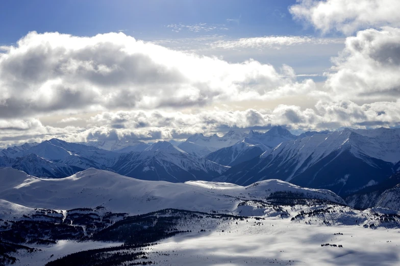 a man riding skis on top of a snow covered slope, by Doug Wildey, flickr, banff national park, distant clouds, panorama distant view, a cozy