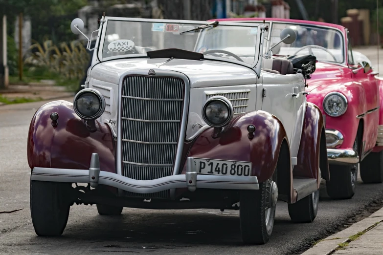 a couple of old cars parked on the side of the road, trending on pixabay, art deco, maroon and white, open top, ford, dynamic closeup