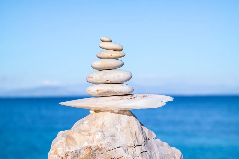 a stack of rocks sitting on top of a rock near the ocean, a marble sculpture, minimalism, relaxed. blue background, tai chi, on a pedestal, clear and focused