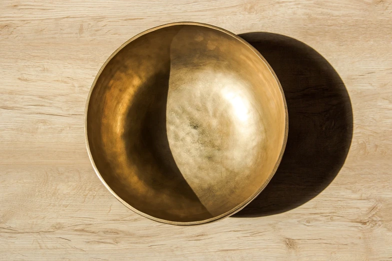 a metal bowl sitting on top of a wooden table, inspired by Gong Kai, unsplash, minimalism, brass instruments, bright dappled golden sunlight, high detail product photo, bottom - view