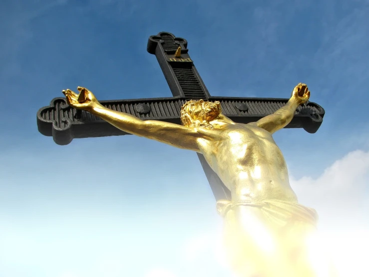 a statue of jesus on a cross against a blue sky, by Jon Coffelt, unilalianism, gold and black metal, bottom - view, shiny gold, bursting with holy light