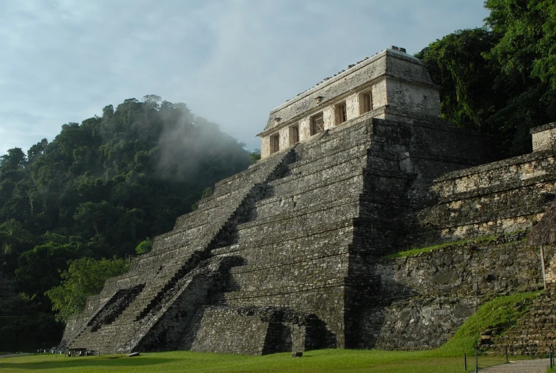 a large stone structure sitting on top of a lush green field, flickr, mayan style, veiled in mist, steps, monumental mountains