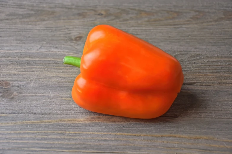 an orange pepper sitting on top of a wooden table, a picture, close-up product photo