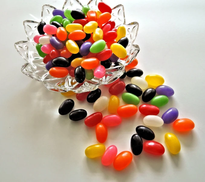 a bowl filled with jelly beans on top of a table, by Joy Garnett, black on white background, beautiful smooth oval head, a table full of candy, colorful plastic