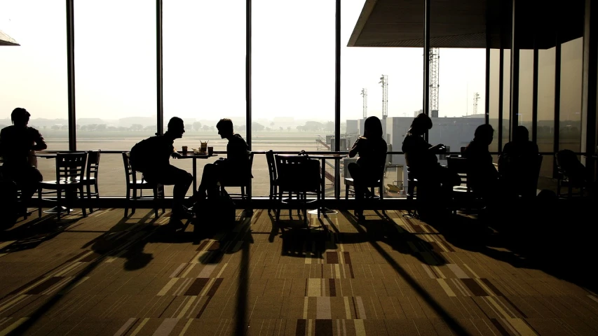 a group of people sitting around a table, by Matt Stewart, pexels, airport, view, deserted, silhouetted