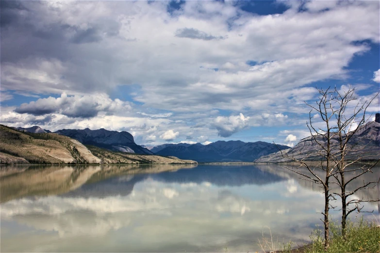 a large body of water with mountains in the background, a photo, by Nancy Carline, shutterstock, drumheller, calm clouds, water mirrored water, beautifully painted