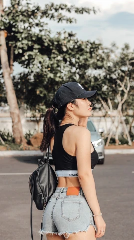 a woman standing in the middle of a parking lot, a picture, inspired by Ion Andreescu, trending on dribble, wearing a backwards baseball cap, training bra, vietnamese woman, close up shot from the side