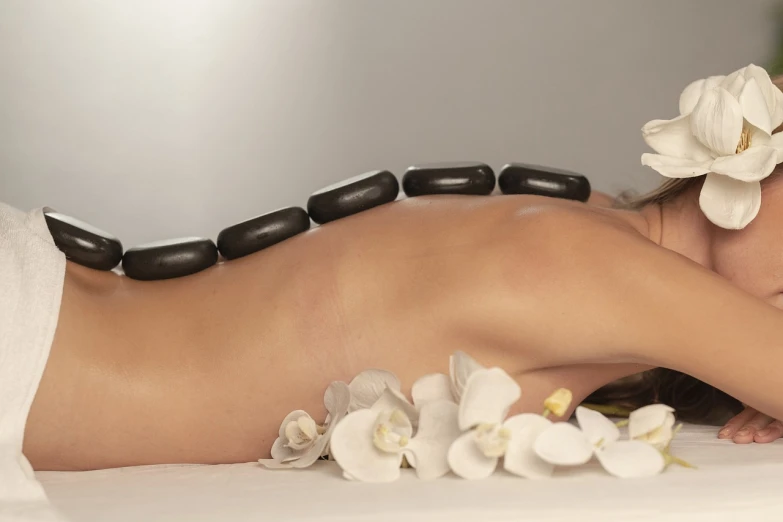 a woman getting a hot stone back massage, massurrealism, posed in profile, flowers, white stones, packshot