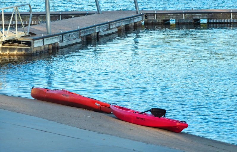 a red kayak sitting on the shore of a lake, a photo, by Linda Sutton, shutterstock, fine art, manly, near a jetty, summer morning, mid shot photo