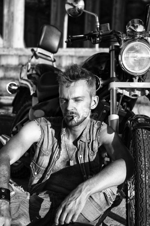 a man sitting on the ground next to a motorcycle, a photo, inspired by Adrian Zingg, wearing a vest top, close - up portrait shot, disheveled, matej ‘retro’ jan