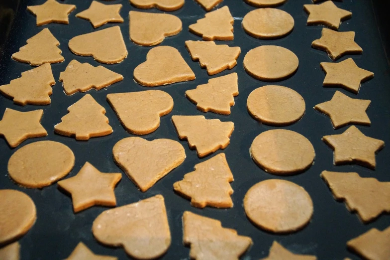 a pan filled with cut out cookies on top of a table, a picture, pexels, folk art, sharp shapes, pets, on a black background, work in progress