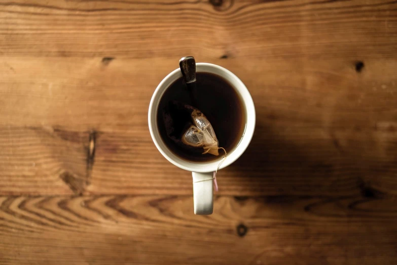 a cup of coffee sitting on top of a wooden table, by Adam Chmielowski, purism, drinking tea, high angle close up shot, infused with a dream, about to consume you