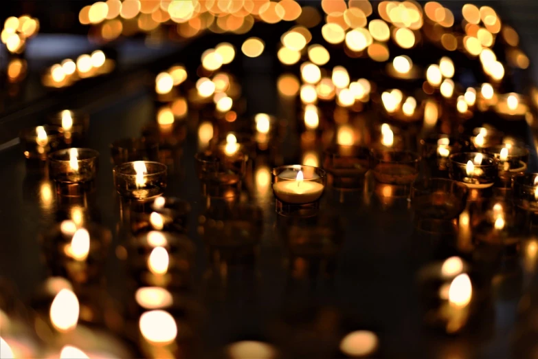 a group of lit candles sitting on top of a table, a picture, by Bernard Meninsky, pexels, golden heavenly lights, bokeh. debadged, many reflections, praying