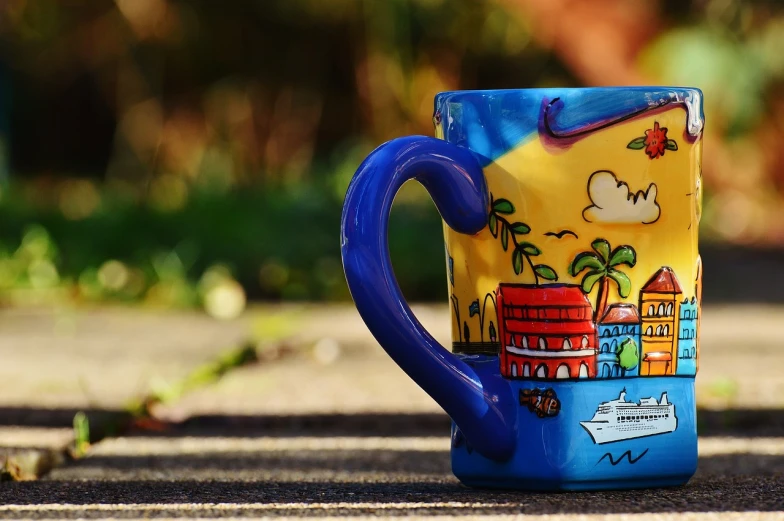 a blue and yellow coffee cup sitting on top of a sidewalk, a picture, pixabay, paradise in the background, cartoon brew, ceramic, port