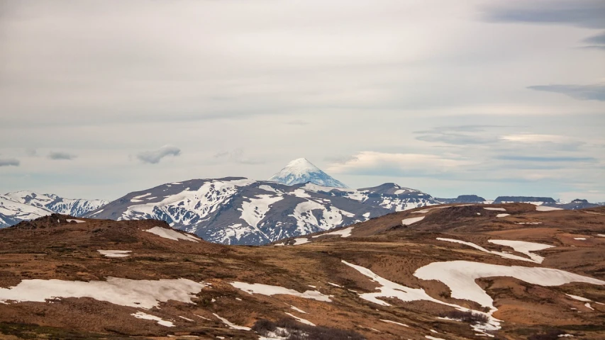 a man flying a kite on top of a snow covered mountain, a picture, by Andrei Kolkoutine, unsplash, hurufiyya, iceland hills in the background, summer landscape with mountain, taiga landscape, spring winter nature melted snow