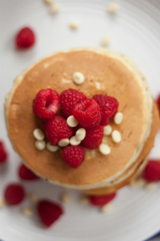 a white plate topped with pancakes and raspberries, romanticism, 35 mm product photo”, close-up shot taken from behind, alex boyd, “organic