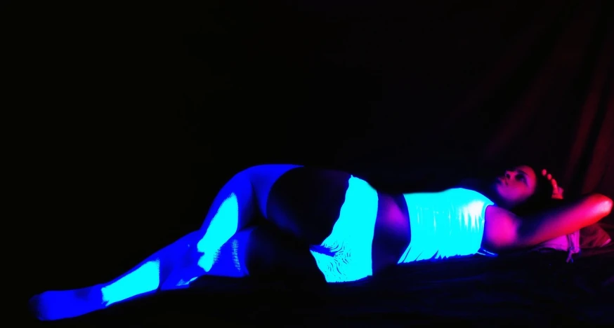 a woman laying on top of a bed under a blue light, tumblr, bodypaint, high contrast backlight, bottom shot, radiation glow