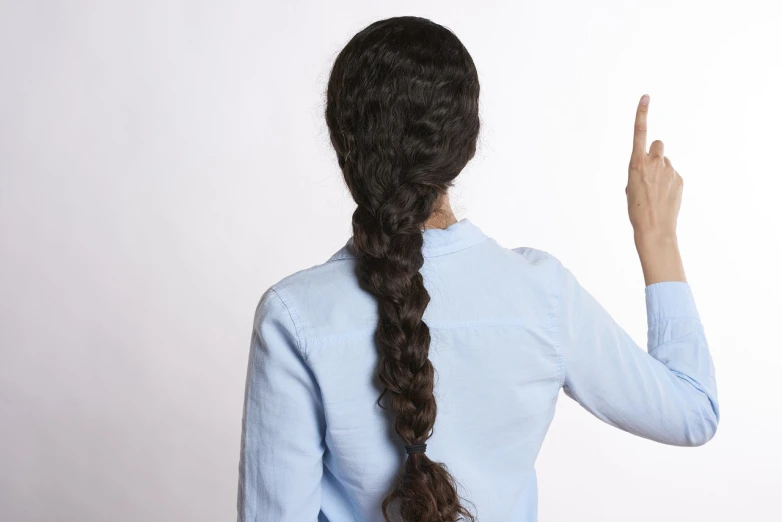 a woman in a blue shirt is pointing at something, by John Luke, shutterstock, realism, long braided curly brown hair, 3 / 4 back view, hands straight down, loose white braid