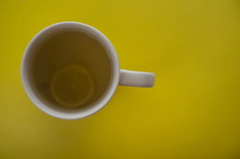 a cup of tea with a lemon slice in it, a stock photo, by Andrew Domachowski, minimalism, yellow background, taken with a pentax k1000, pareidolia, flying shot