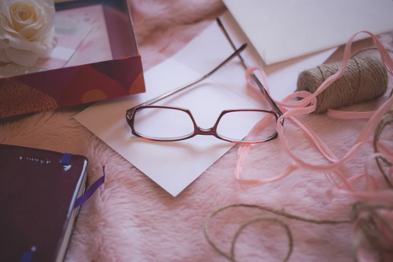 a pair of glasses sitting on top of a pink blanket, a picture, romanticism, writing a letter, bows, close-up shot, card