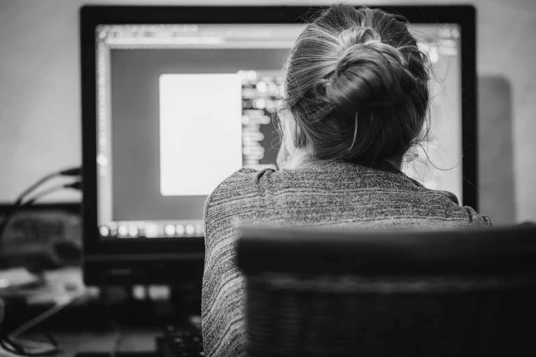 a woman sitting in front of a computer monitor, a black and white photo, by Adam Marczyński, pexels, long shot from back, programming, photo of the girl, stacked image