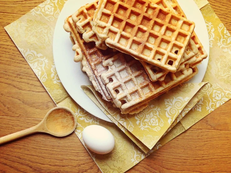 a white plate topped with waffles next to an egg, by Anna Haifisch, shutterstock, renaissance, warm shading, vintage - w 1 0 2 4, squares, wooden