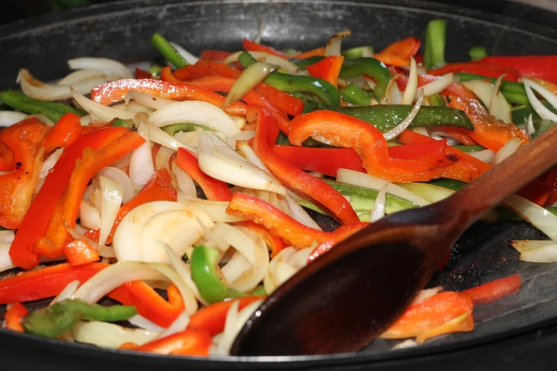 a frying pan filled with vegetables and a wooden spoon, close up photo, sombrero, filleting technique, onions