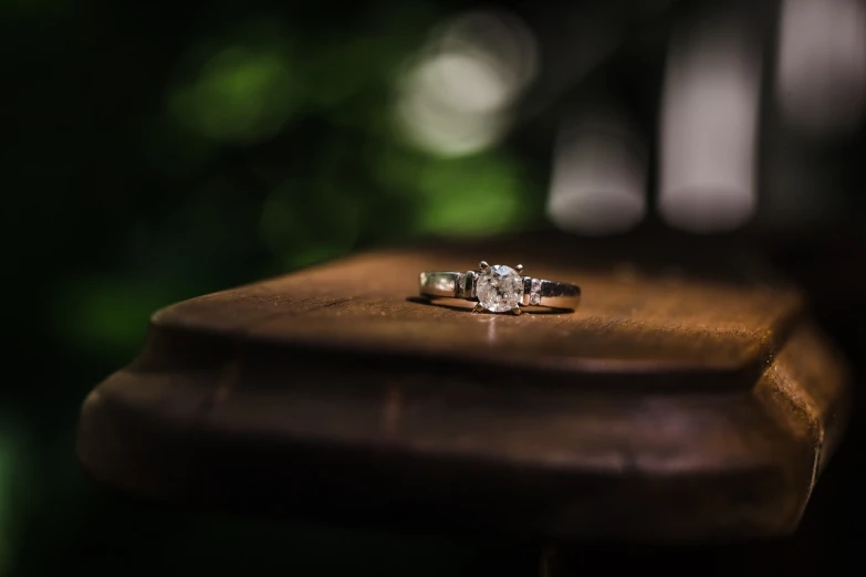 a diamond ring sitting on top of a wooden table, a picture, by Adam Szentpétery, pexels, on a wooden tray, summer evening, furniture photography, against the backdrop of trees