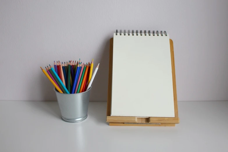 a cup filled with colored pencils next to a notepad, a drawing, visual art, large vertical blank spaces, on a pale background, product introduction photo, whiteboards