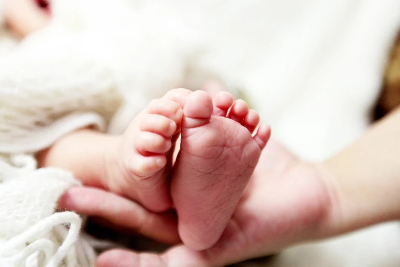 a close up of a person holding a baby's foot, incoherents, superior quality, advanced technology, lots of light, multi - layer